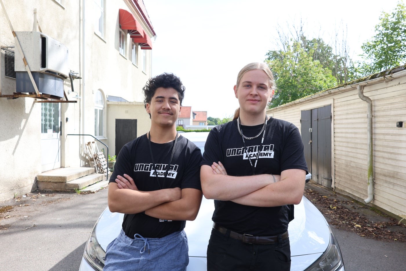 Ángel Garcia och Erik Rosell med armarna i kors framför en vit bil, båda i svarta UngDrive Academy-tröjor
