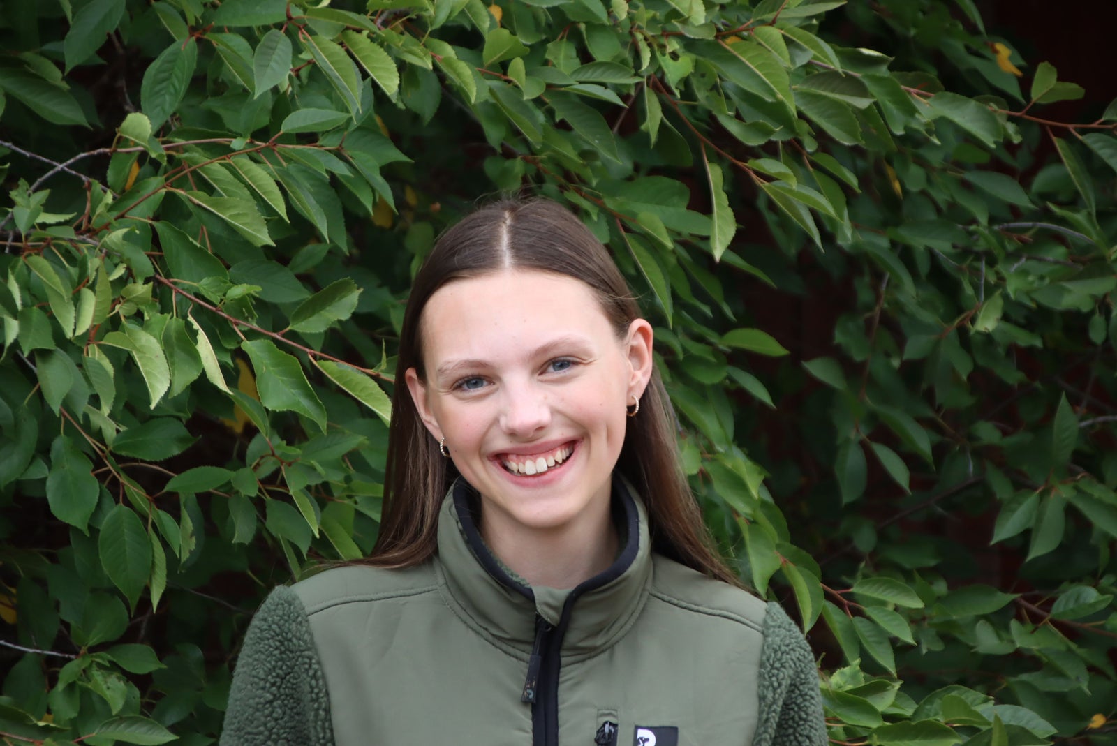 Linnea Fridberger utomhus, leende framför grönskande lövverk