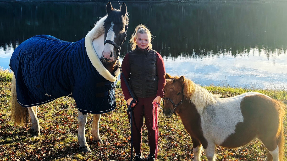 Emmy Jalar står med två hästar vid en sjö